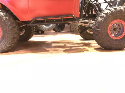 1989 Ford Bronco - The underside of a red RC rock crawler, showing its suspension and off-road tires, with another crawler in the background.