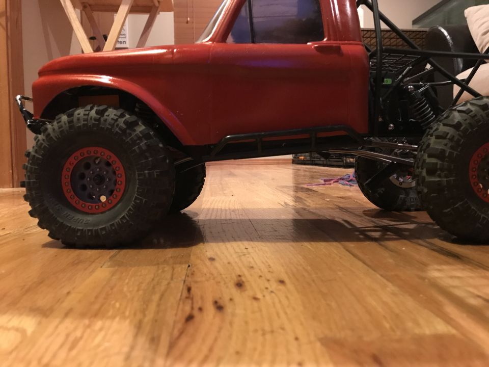 Red RC truck side view with large off-road tires and roll cage