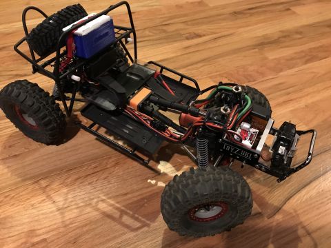 1989 Ford Bronco - This RC rock crawler chassis is shown from a three-quarter front angle on a wooden surface.