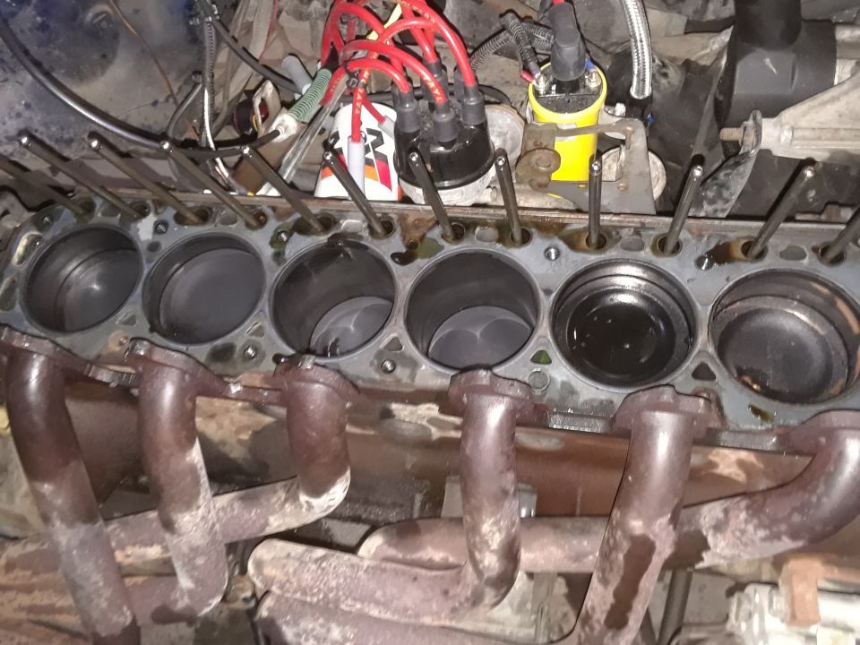 Engine block with six cylinders, pistons visible, and exhaust manifold attached. Some red spark plug wires are present
