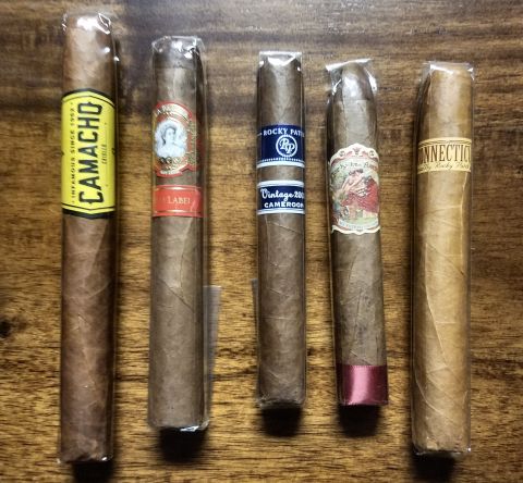 2018 Ford Bronco - Collection of five cigars from various brands, including Camacho and Rocky Patel, displayed on a wooden surface.