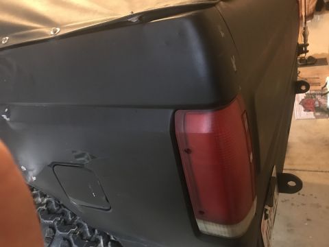 1989 Ford Bronco - The rear quarter panel and tail light assembly of a black Ford Bronco are visible, with a soft top covering the upper portion.
