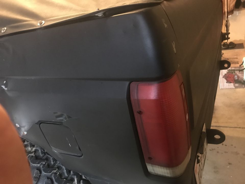 Close-up of a black Ford Bronco's rear tail light and quarter panel. The vehicle has a soft top cover