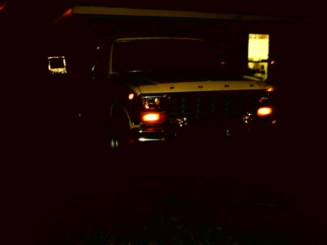 Front view of a dark 1978 Ford F-Series truck with headlights on