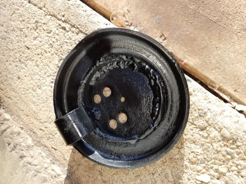 1995 Ford Bronco - A black brake drum with rough welds and several bolt holes sits on a textured surface.