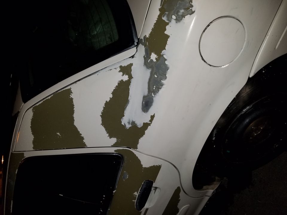 Side view of a white car with peeling paint showing primer and olive drab underneath