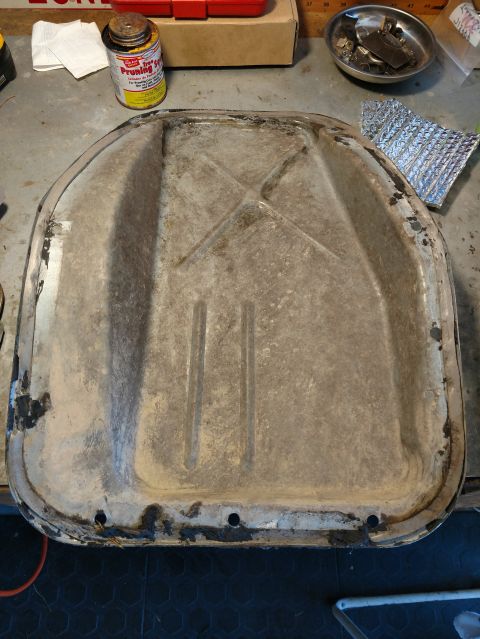1992 Ford Bronco - A metal heat shield, possibly for a vehicle, is shown on a workbench with various tools and supplies in the background.