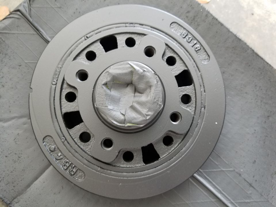 Gray crankshaft pulley with tape over the center, showing stamped numbers 'CM 8318' and 'RB4 O'