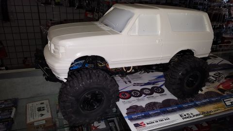 1996 Ford Bronco - An unpainted RC car body resembling a Ford Bronco sits on a display mat with tire options.