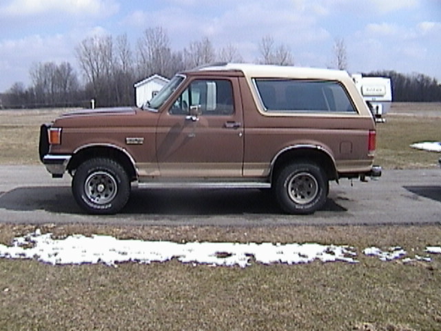 Brown two-tone Ford Bronco, side profile parked on pavement with patchy snow on grass