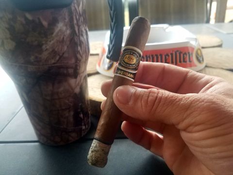 2018 Ford Bronco - A hand holds a cigar with a band that reads 'Romeo y Julieta 1875 Anniversary' next to a camouflage cup and an ashtray.