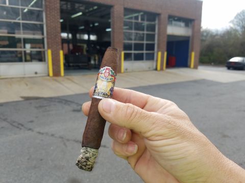 2018 Ford Bronco - A person is holding a lit cigar in front of a building with garage doors. The cigar has a band that says "American" and "Alec Bradley".