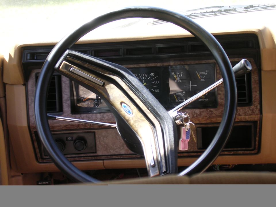Tan 1980s Ford truck dash and black steering wheel with woodgrain gauge bezel, keys in ignition