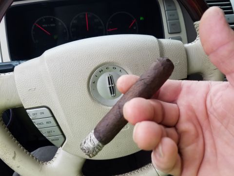 2018 Ford Bronco - A hand holds a cigar in front of a car's steering wheel and dashboard. The steering wheel has a Lincoln logo in the center.