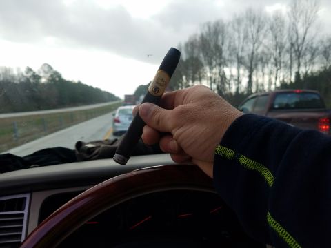 2018 Ford Bronco - A hand holds a cigar over the dashboard of a vehicle while driving on a highway. The steering wheel and dashboard gauges are visible in the…