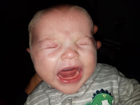 2018 Ford Bronco - A close-up photo of a baby crying with its eyes closed and mouth open. The baby is wearing a gray and white striped onesie with a green din…