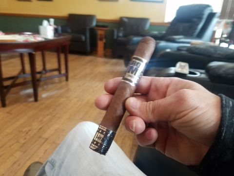 2018 Ford Bronco - A person holds a cigar with a silver and black band in their hand. The background shows a room with wooden floors, chairs, and a table.
