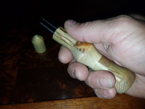 2018 Ford Bronco - A hand holds a wooden tool with two metal prongs. A small wooden cap sits on a dark wooden surface next to it.