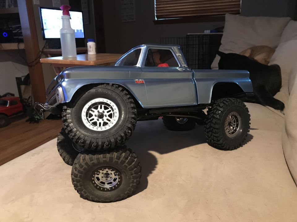 Light blue RC pickup truck with large off-road tires stacked on tires, on a couch.