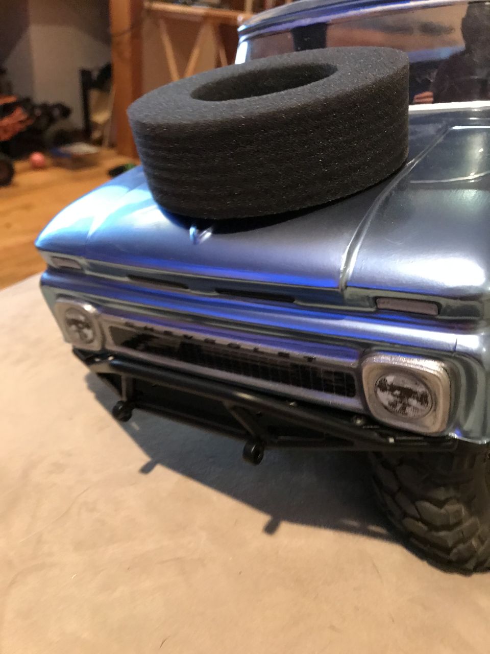 Metallic blue RC truck front with black foam tire insert on hood, grille, headlights, and bumper.