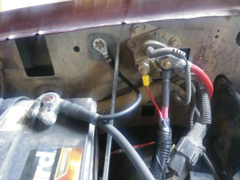 1996 Ford Bronco - The image shows a close-up view of a vehicle's engine bay, focusing on the battery and starter solenoid connections. A red cable runs from…