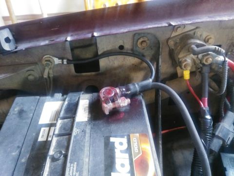 1996 Ford Bronco - A close-up view of a car battery and its associated electrical connections, including a starter solenoid mounted on the vehicle's firewall.