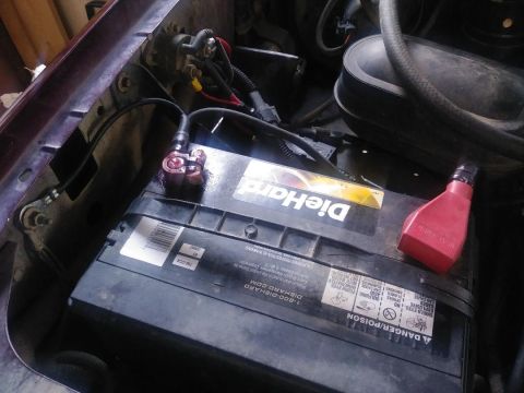 1996 Ford Bronco - A close-up view of a DieHard car battery in an engine bay, with a red battery terminal protector and a black cable connected to the positiv…