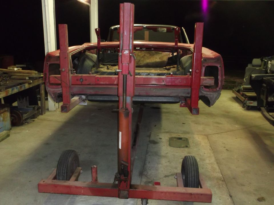 Red car body on a rotisserie lift in a garage, interior stripped.