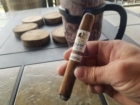 2018 Ford Bronco - A person's hand holds a lit cigar with a "Rogue Rascal" band in front of a mug and several wooden coasters on a table.