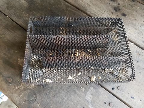 2018 Ford Bronco - A burnt metal mesh basket sits on a wooden surface. The basket is rectangular with a perforated design and appears to have residue inside.