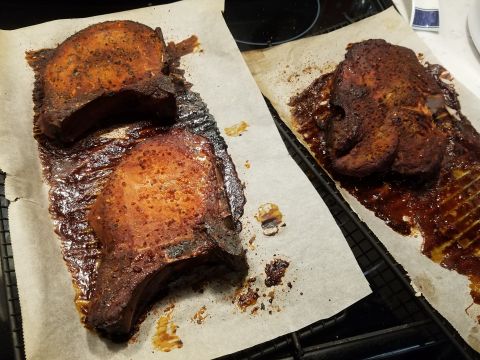 2018 Ford Bronco - Two thick-cut pork chops are seasoned and cooked, resting on parchment paper on a cooling rack. The pork chops are glazed with a dark, stic…