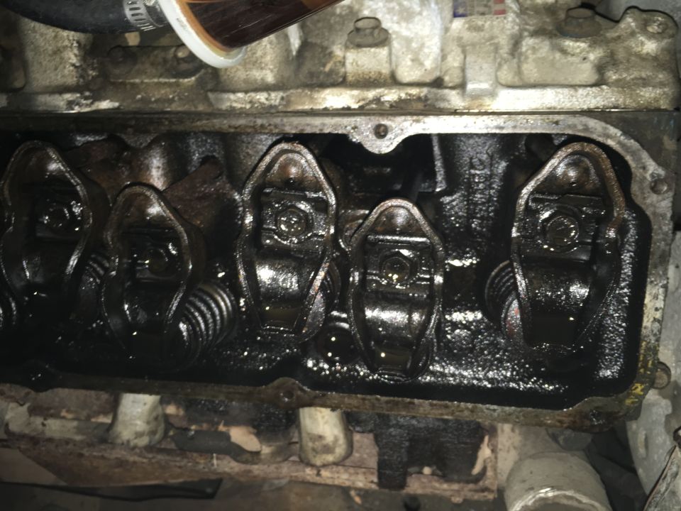 Engine valve cover interior with rocker arms and springs covered in oil.