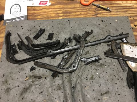 1980 Ford Bronco - A pile of old, greasy, broken gasket pieces and a metal scraper are laid out on a gray absorbent mat on a wooden surface. A portion of a ma…