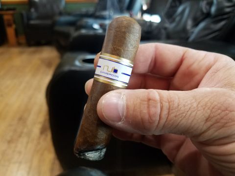 2018 Ford Bronco - A hand holds a lit cigar with a band that reads "NJ" and "CAMEROON". The background is blurred and shows dark leather seating and wooden fl…