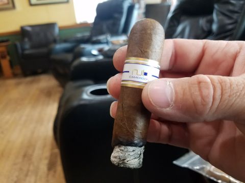 2018 Ford Bronco - A person is holding a lit cigar with a band that reads "NUB CAMEROON". The background shows a lounge area with leather chairs.