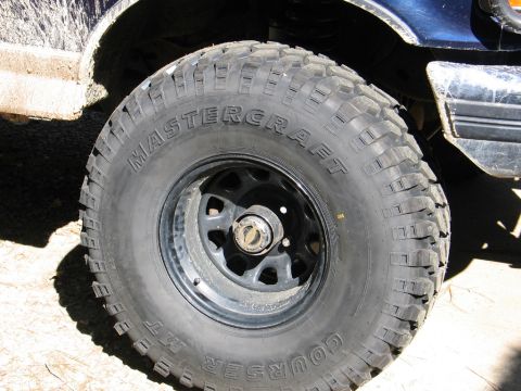 1995 Ford Bronco - Close-up of a Mastercraft Courser MT tire and black rim on a dirty blue vehicle.