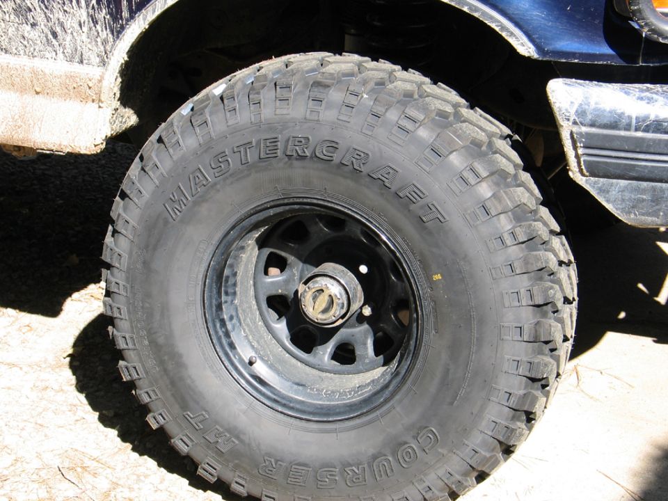 Mud-splattered blue vehicle fender above a Mastercraft Courser MT tire on a black rim