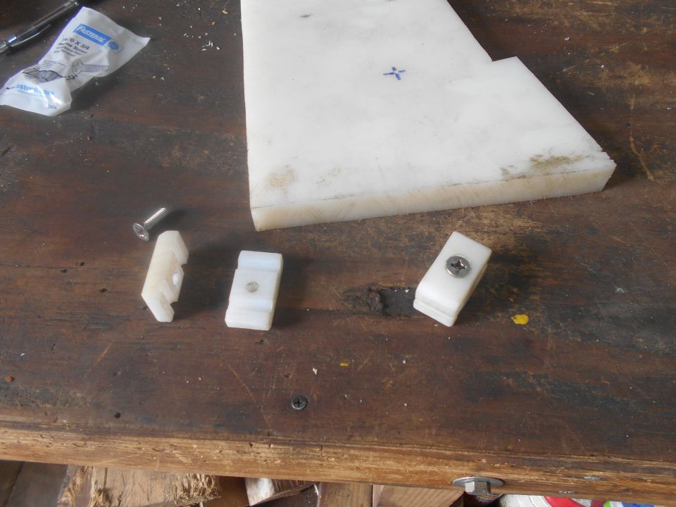 White plastic sheet with blue cross, small plastic parts, and screws on a wooden workbench.