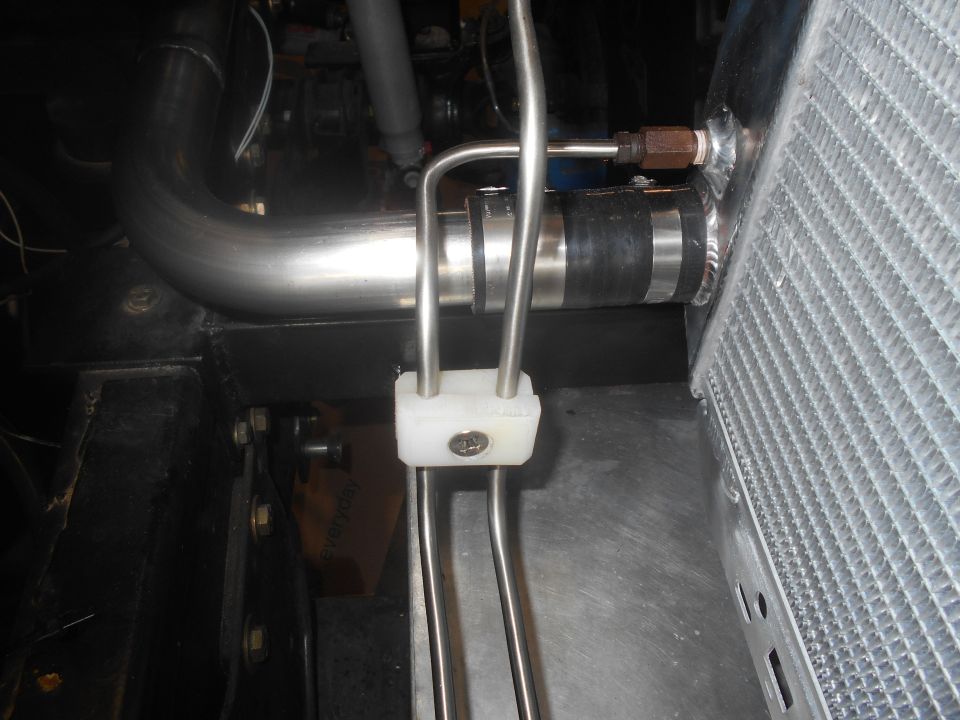 Close-up of radiator hose connection with white bracket and metal rods.