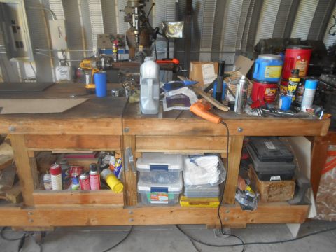 1992 Ford Bronco - A cluttered workbench in a garage setting is filled with various tools, spray cans, and storage containers. A milling machine is visible in…