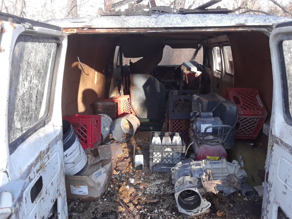 Interior of a white van filled with junk, including crates, buckets, and mechanical parts.