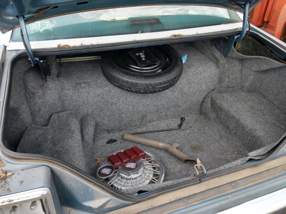 Open trunk of a blue sedan showing spare tire, jack, hubcap, and red taillight lens.