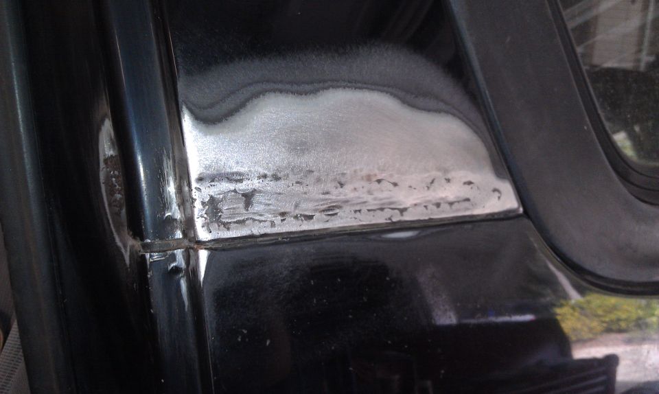 Close-up of metal repair work on a black car door frame with visible rust and primer
