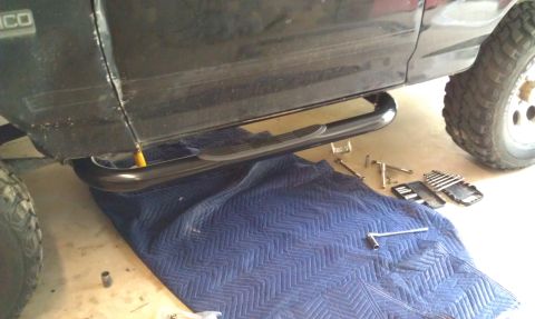 1995 Ford Bronco - A black SUV with a running board installed is shown from the side. Tools and a blue moving blanket are laid out on the ground beneath the v…
