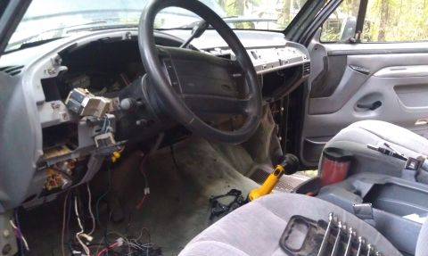 1995 Ford Bronco - The interior of a vehicle shows a disassembled dashboard with exposed wiring and a steering wheel.