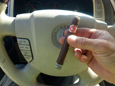 2018 Ford Bronco - A hand holds a lit cigar in front of the steering wheel of a car, with the dashboard gauges visible in the background.