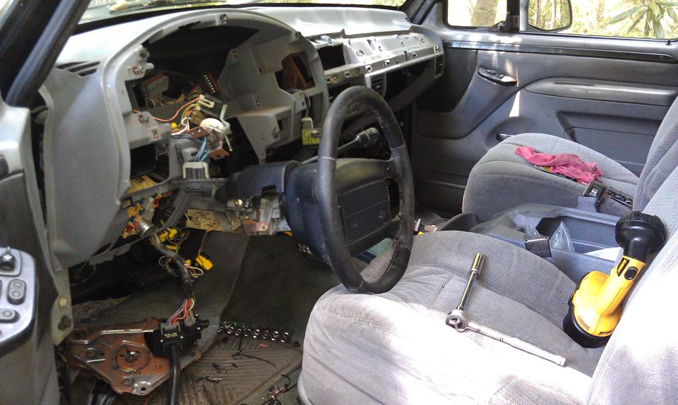 1995 Ford Bronco interior with dashboard removed, showing wiring and components. Steering wheel and seats are visible