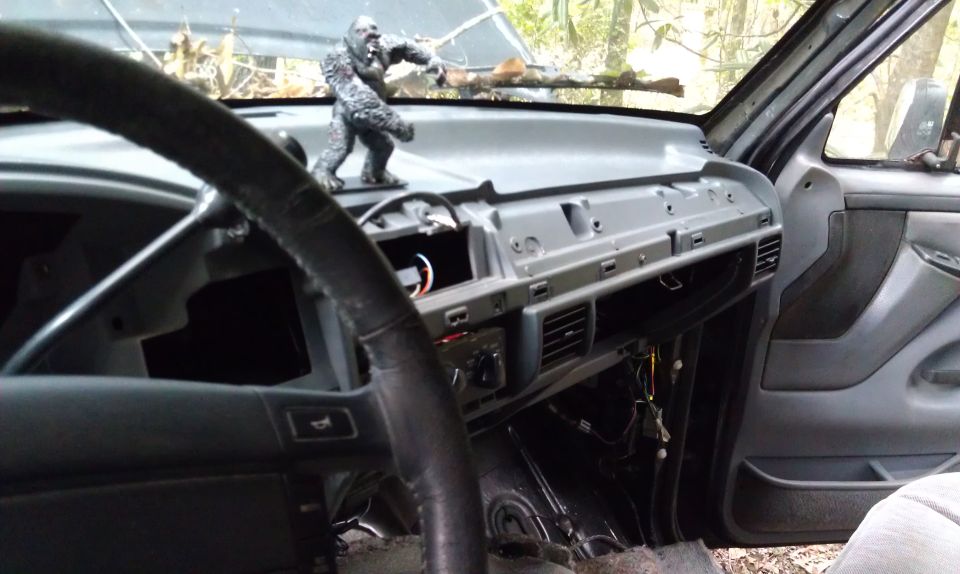 Dashboard of a disassembled vehicle, showing exposed wiring and a gorilla figurine on the dash