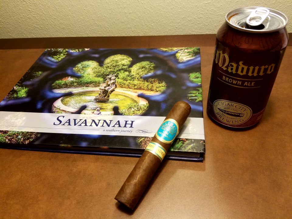 Book titled Savannah, a cigar, and a can of Maduro Brown Ale on a brown surface