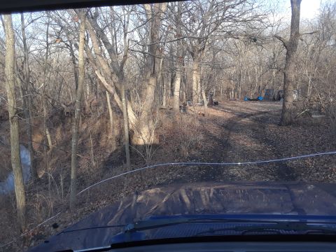 1985 Ford Bronco - View from inside a vehicle as it travels down a dirt road surrounded by trees in a wooded area.